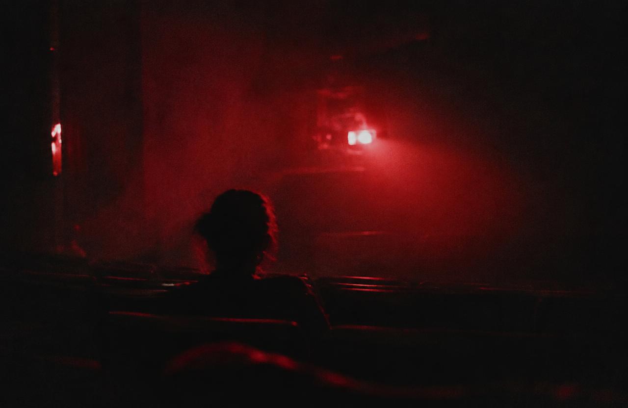 A lone silhouette facing a glowing cinema screen in a dark theater